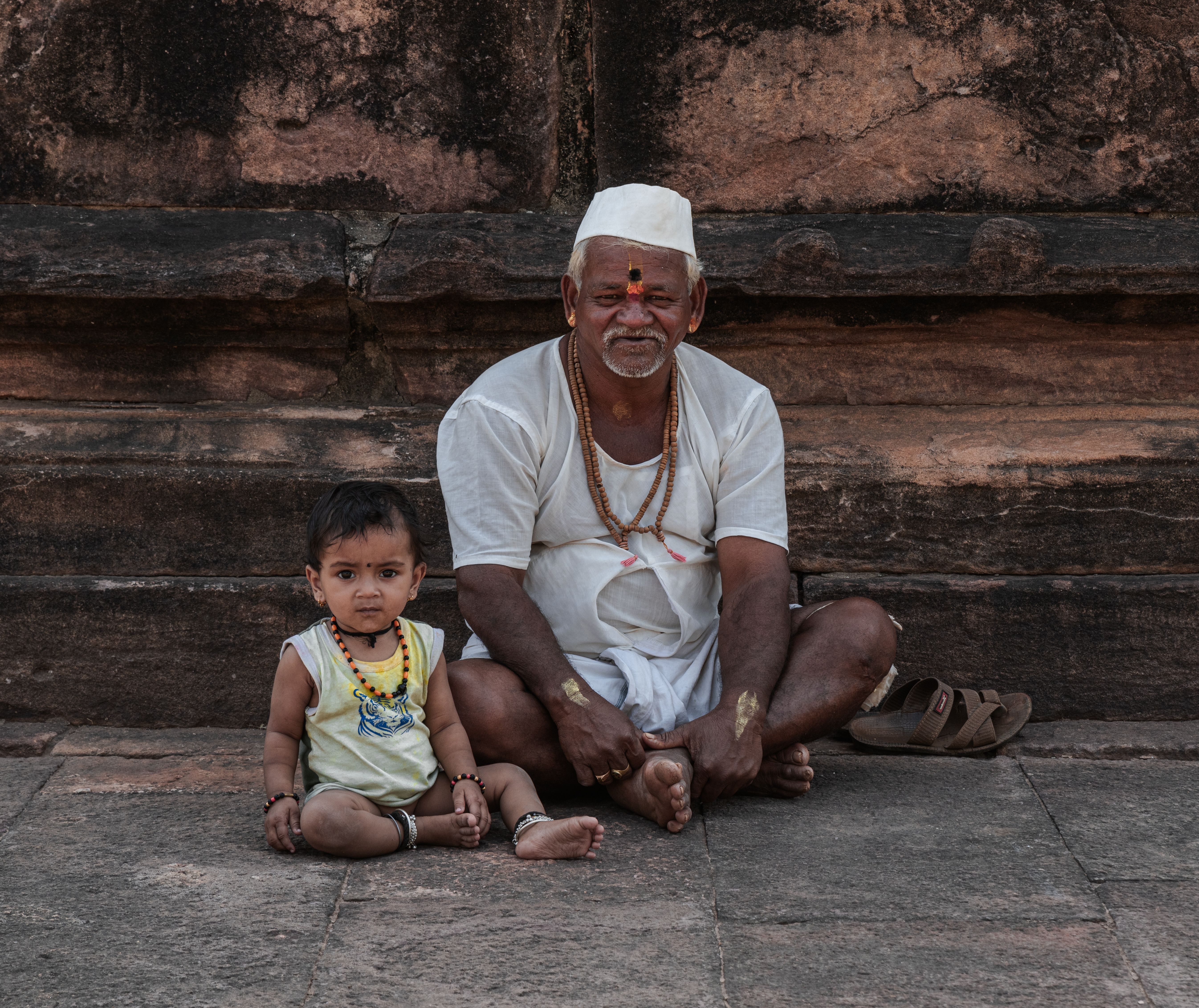 Elderly man and child seated on stone steps in Ayhole, Karnataka, India, capturing cultural essence.