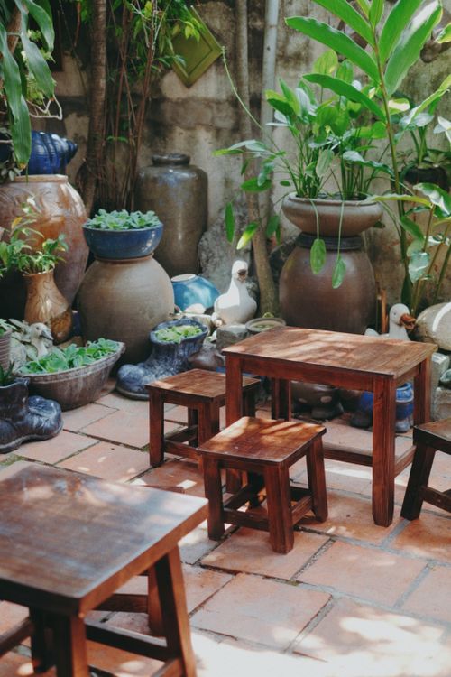 Free Charming garden setting with rustic wooden tables, chairs, and lush green plants. Stock Photo