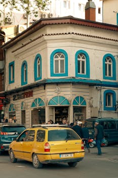 A busy street corner with a yellow car in front of a vintage building and pedestrians.