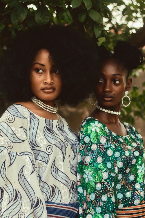 Free Two women in vibrant traditional African attire stand under a tree, exuding elegance and style. Stock Photo