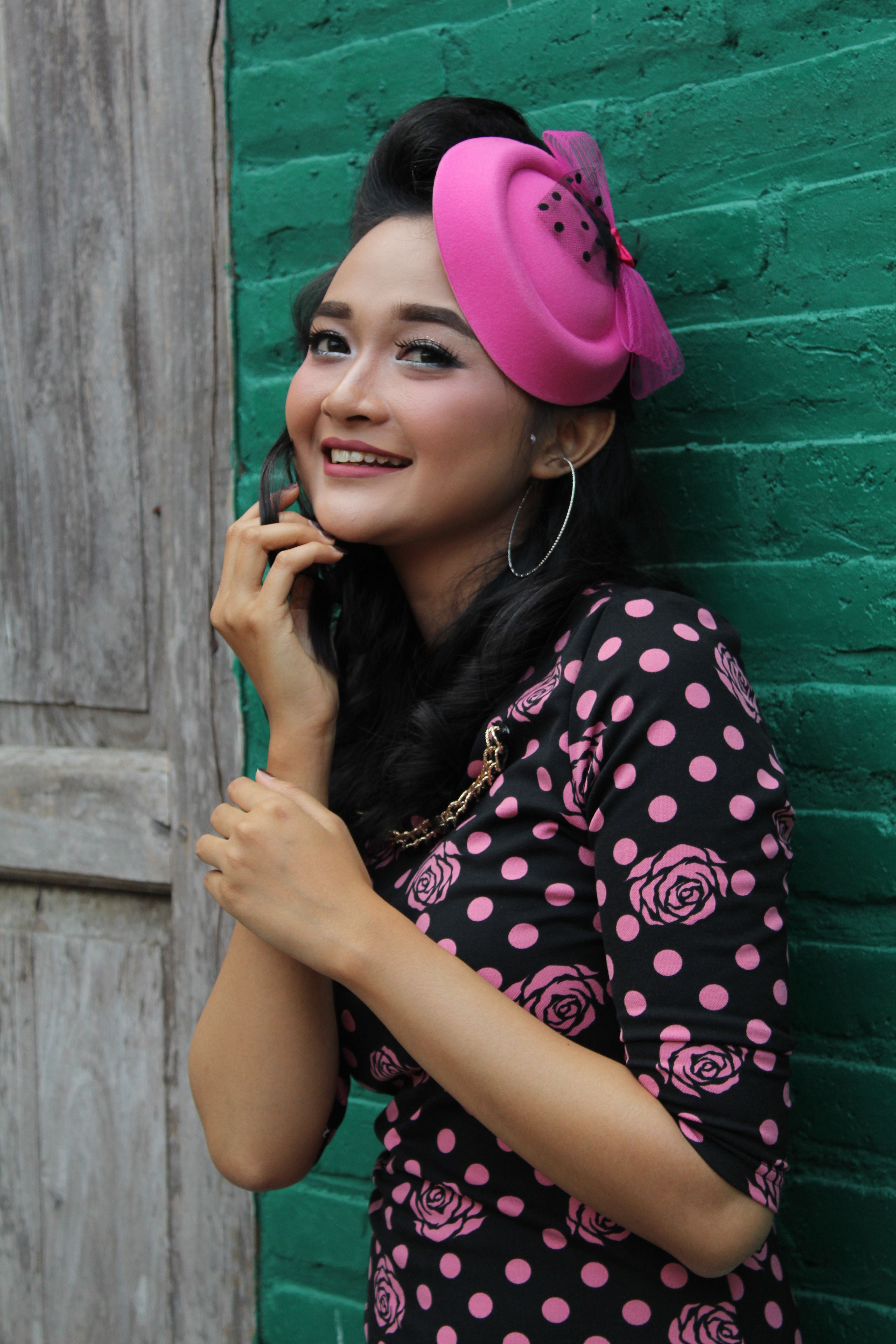 Charming portrait of a woman in vintage attire, smiling against a green wall in Indonesia.