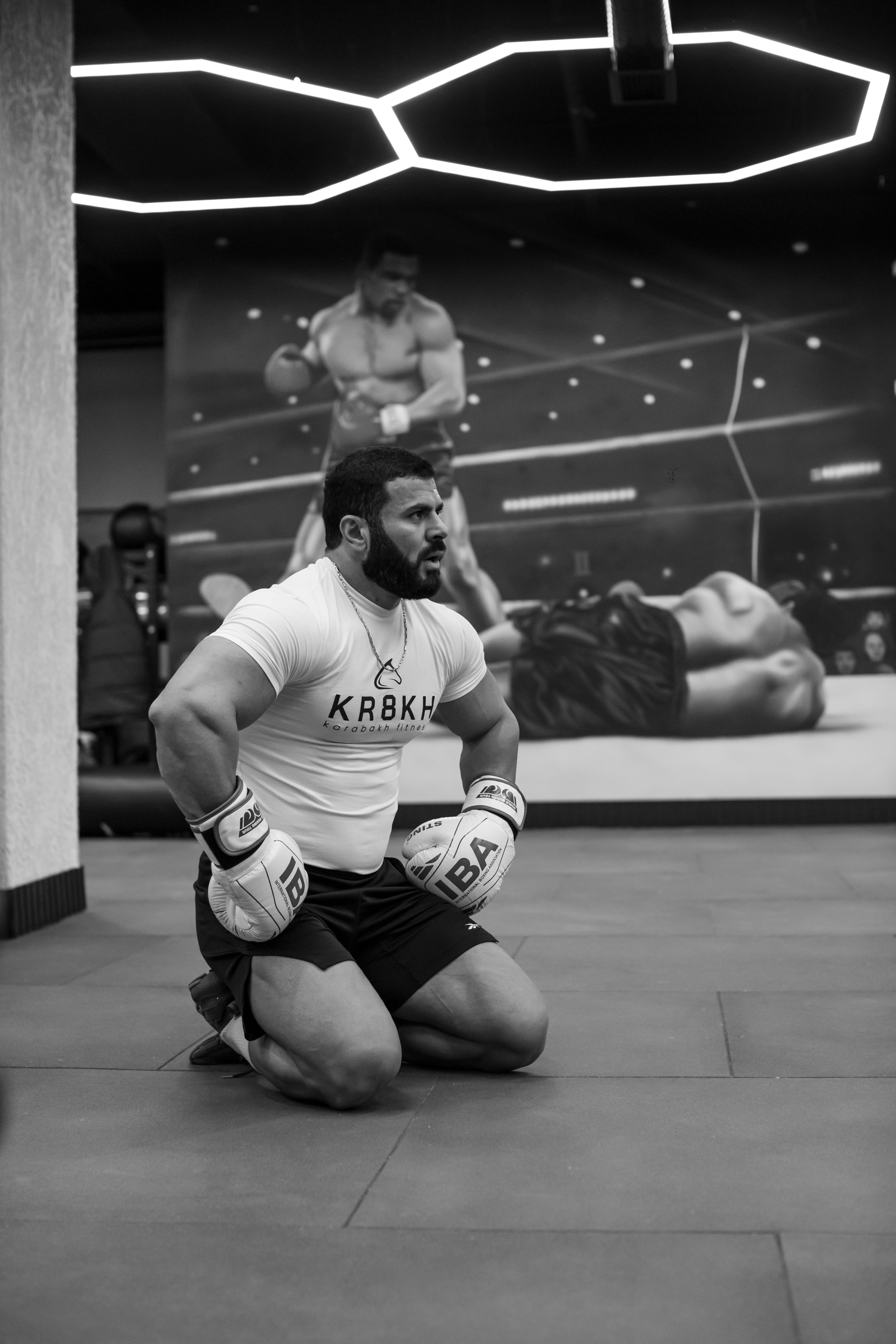 Boxer kneeling in a Baku gym during an intense training session, surrounded by motivational posters.