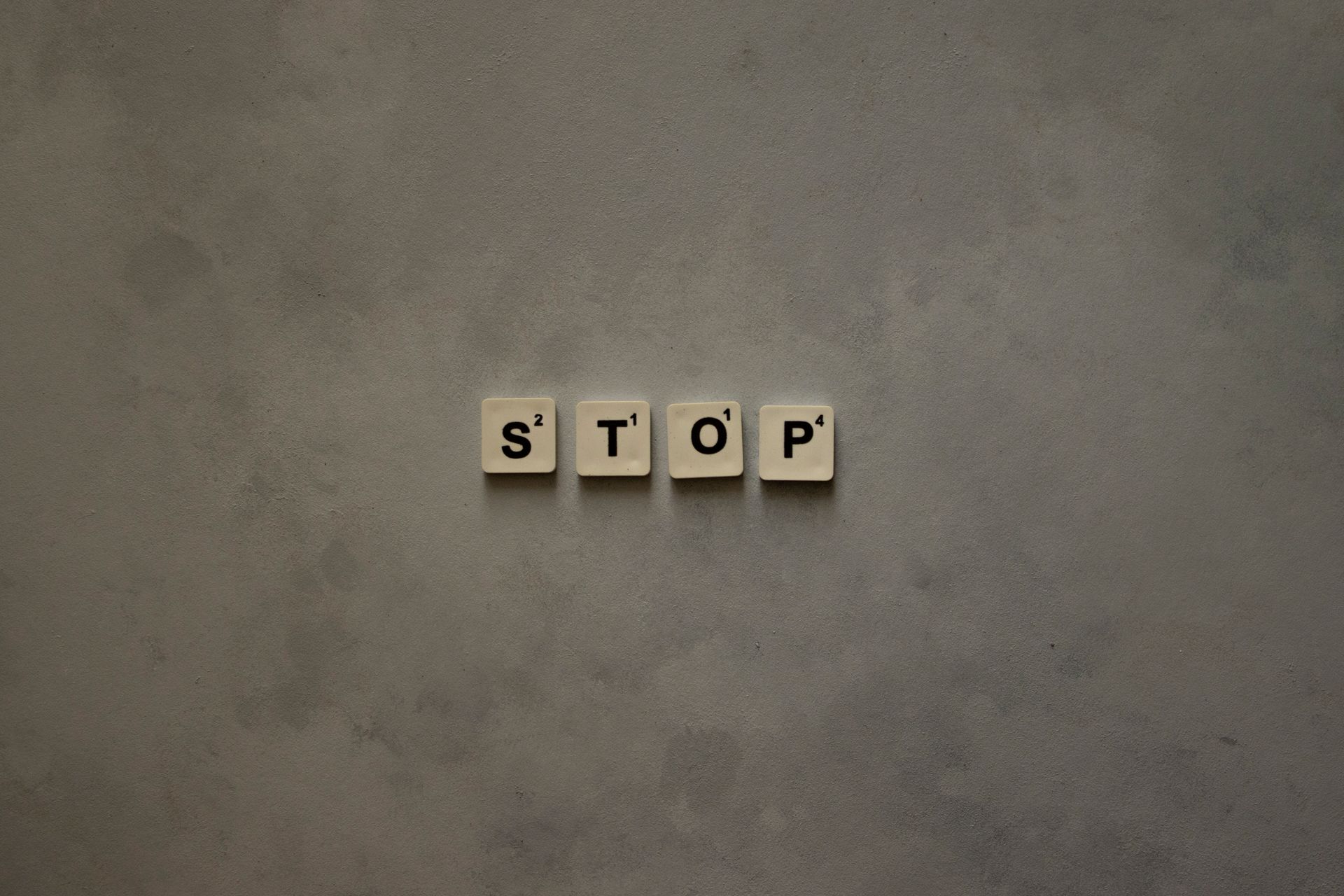 Scrabble tiles spelling STOP against a textured wall surface. Minimalist and conceptual design.
