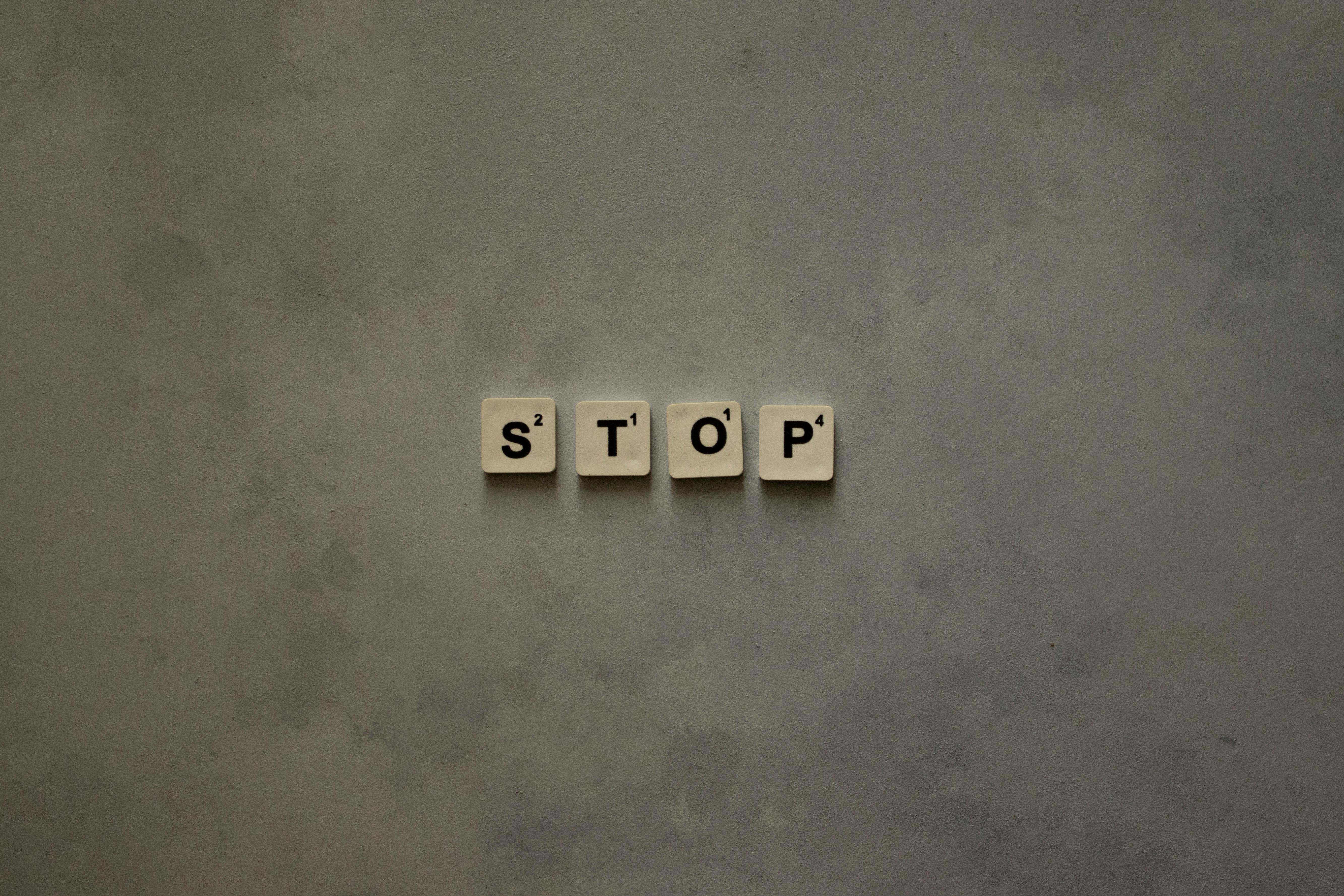 Kostnadsfria Scrabble-plattor som stavar STOP mot en strukturerad väggyta. Minimalistisk och konceptuell design. Stock foto