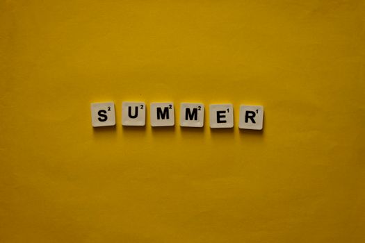 Scrabble tiles spelling 'Summer' on bright yellow background, evoking warmth and joy.