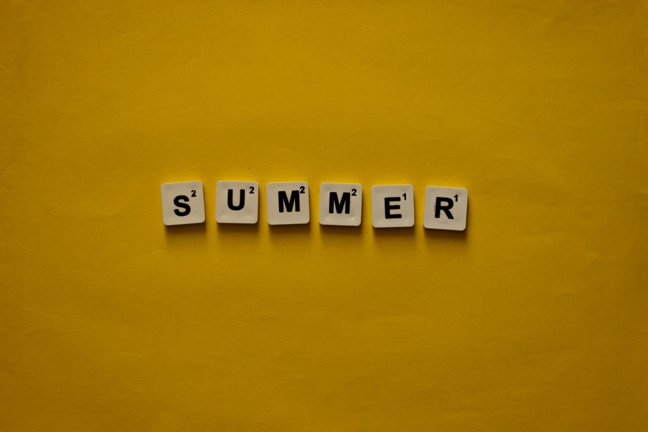 scrabble tiles spelling summer on bright yellow background evoking war