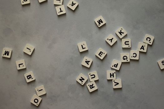 A collection of mixed letter tiles scattered across a textured grey surface.