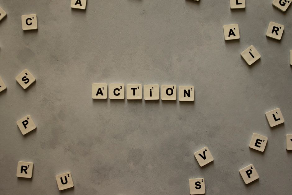 Flat lay of Scrabble tiles spelling ‘Action’ on a gray background, surrounded by random letters.