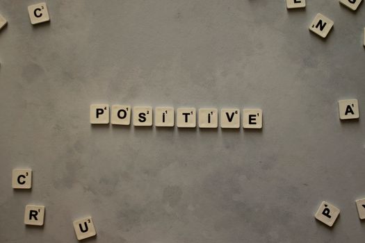 Scrabble tiles arranged to spell 'positive' on a gray textured surface, conveying optimism.