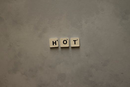 A minimalist composition with Scrabble tiles spelling 'HOT' on a textured gray surface.
