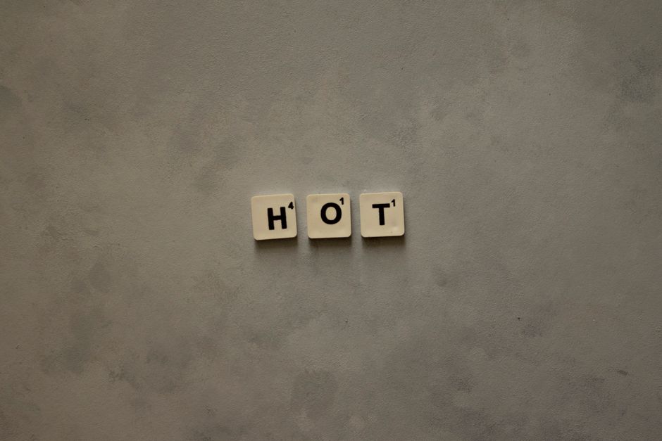 A minimalist composition with Scrabble tiles spelling 'HOT' on a textured gray surface.