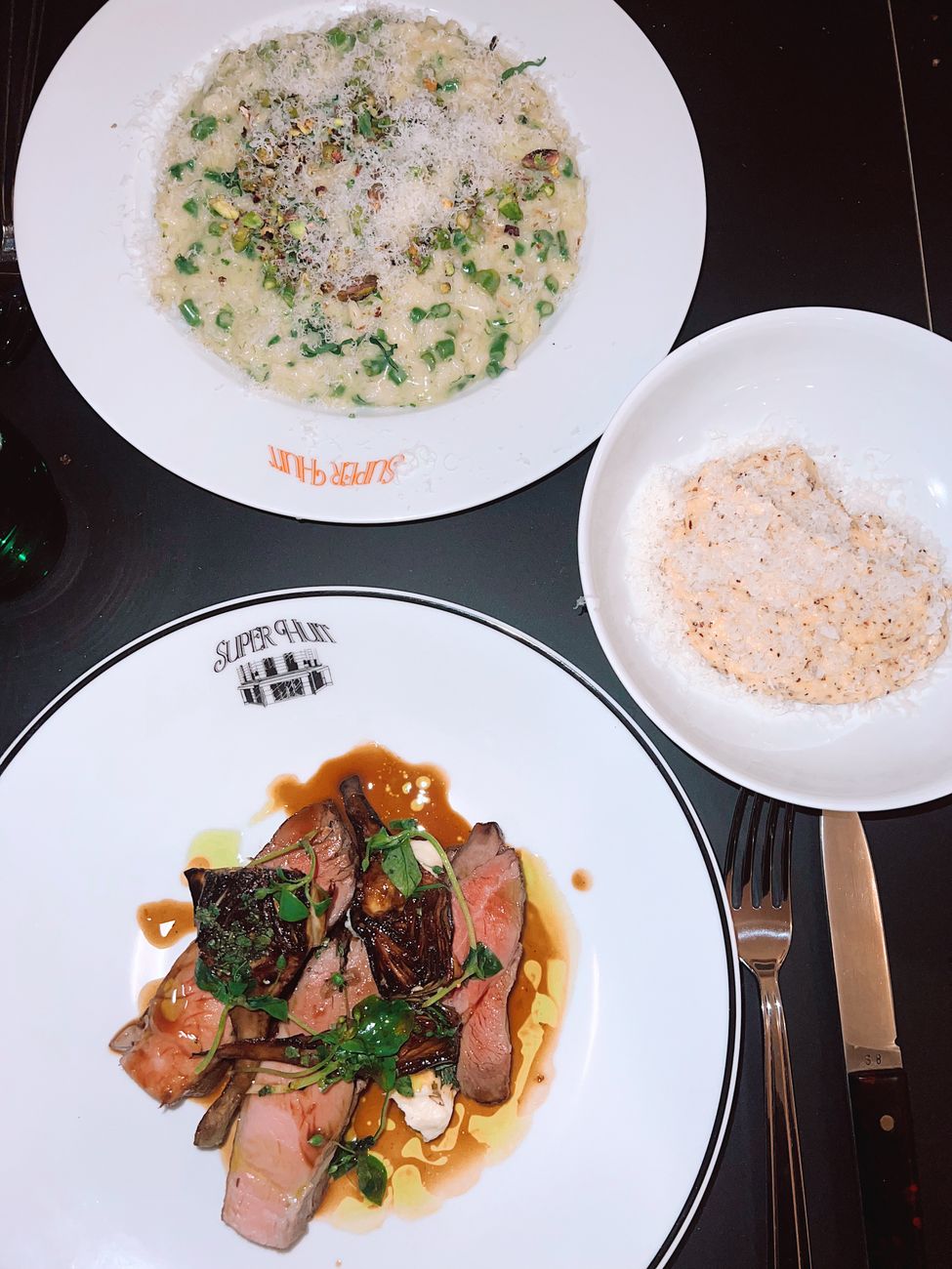 A bowl of creamy white risotto garnished with fresh green herbs and grated pecorino Romano cheese, with a small dish of golden red-tinged scorpion oil alongside