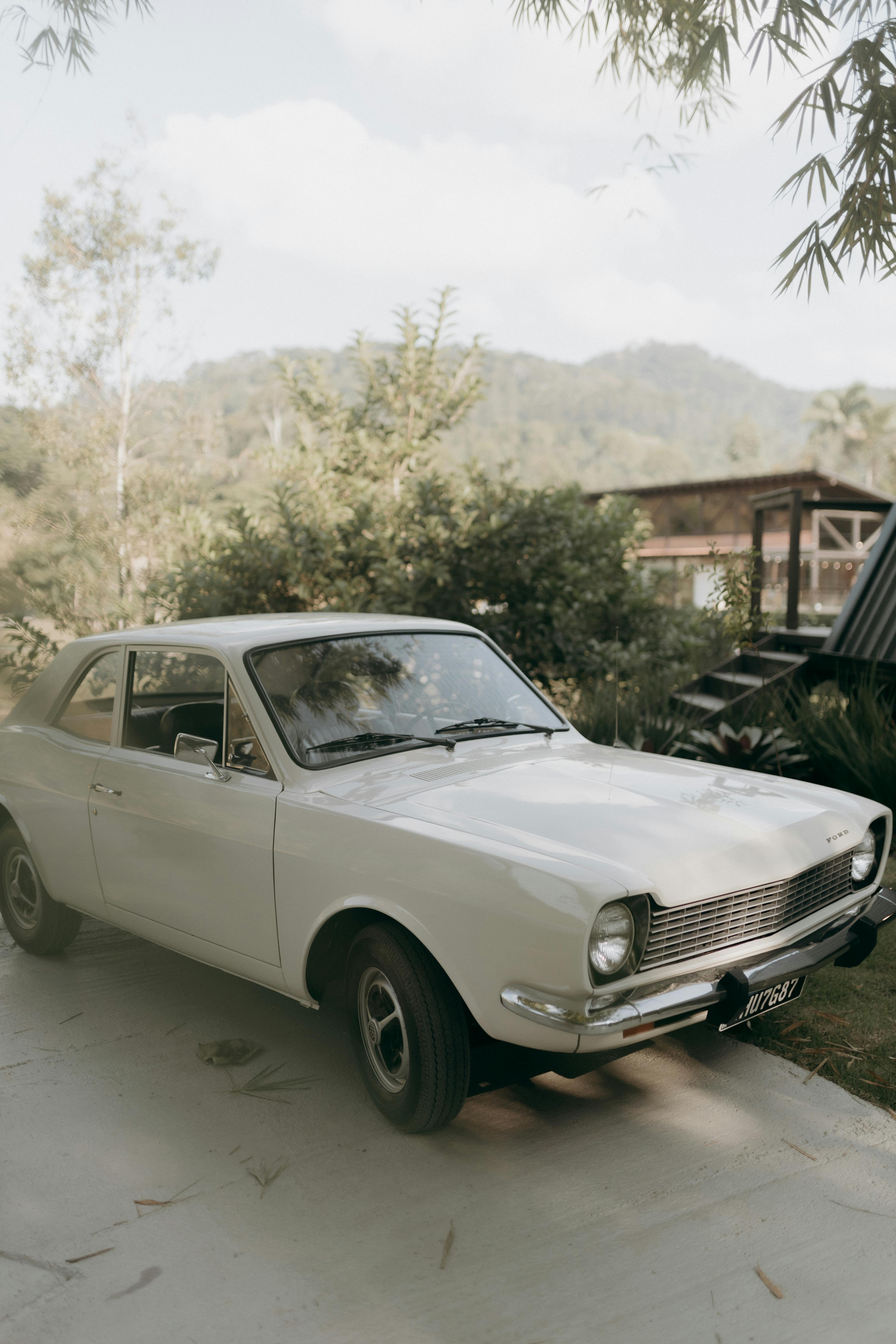 A classic white vintage car parked outdoors with scenic mountain view.
