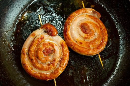 Close-up of spiral sausages frying in a pan, showcasing a delicious, rustic meal preparation.