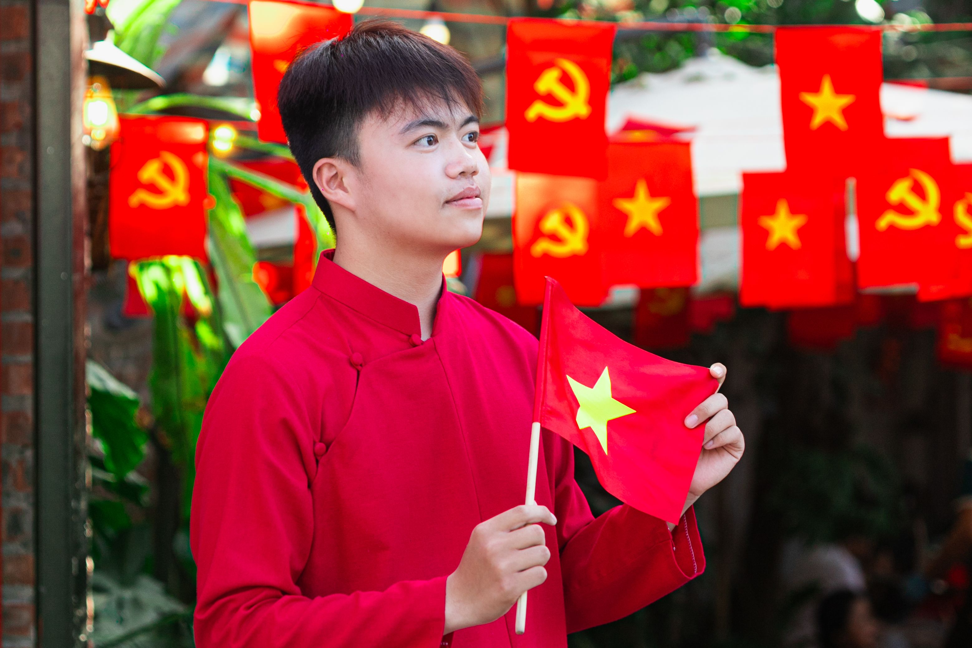 Young man in traditional attire holding Vietnam flag, celebrating National Day with vibrant decorations.