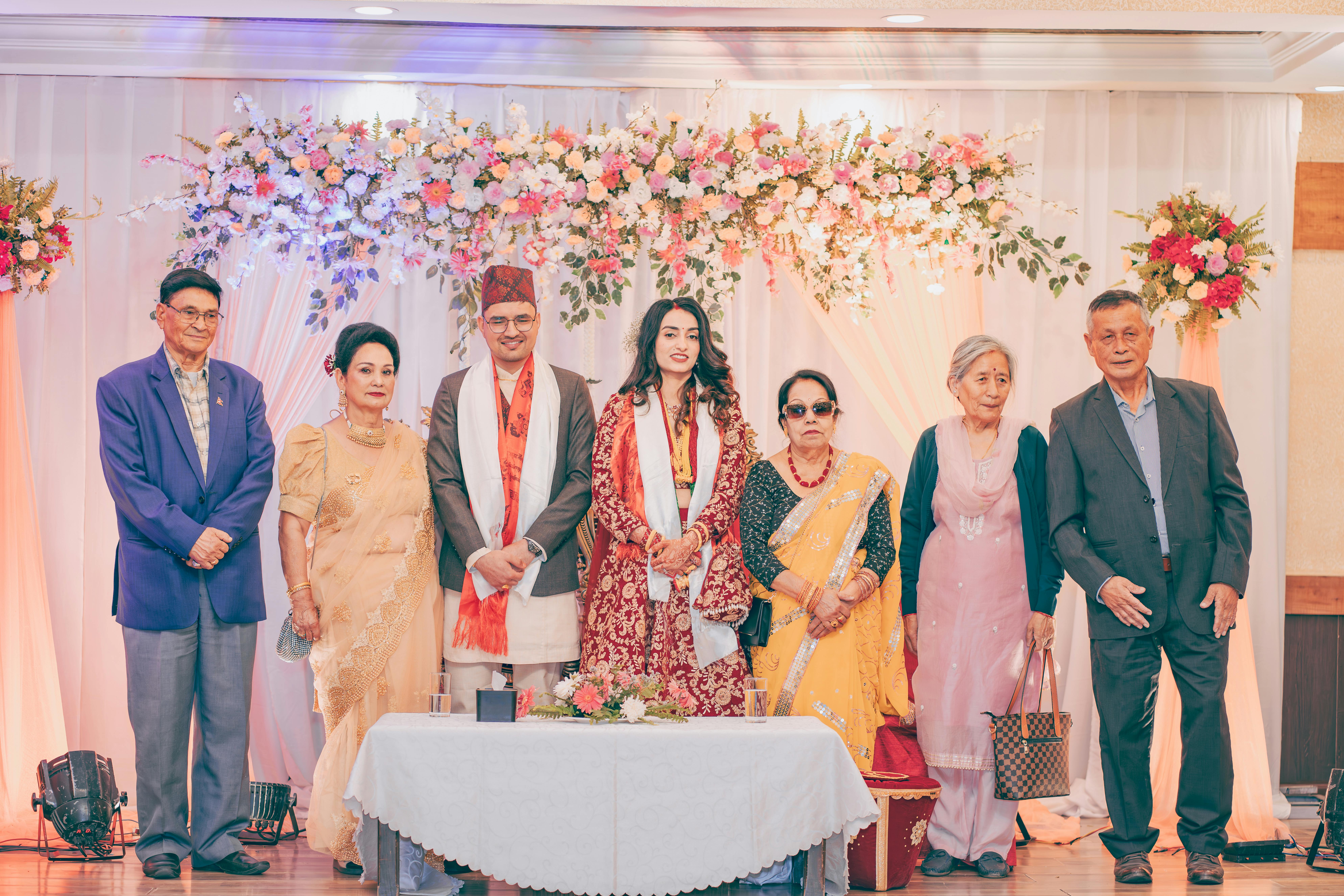 Elegant Nepalese wedding celebration showcasing family members in traditional attire with floral backdrop.