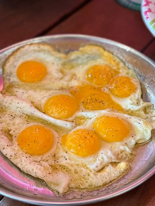 Free A close-up of sunny side up fried eggs seasoned with pepper on a metal plate. Stock Photo