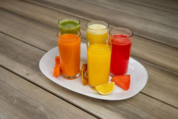 Glasses of carrot, green, orange and watermelon juice on a white plate with cut fruit