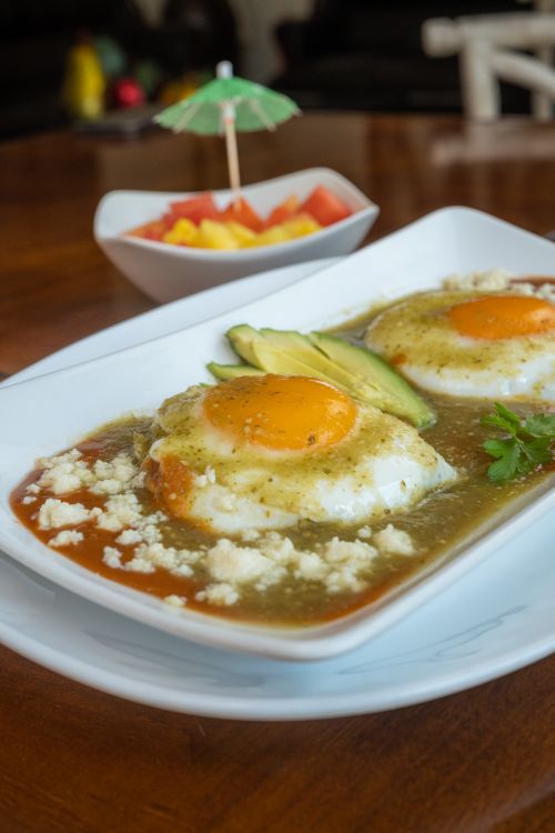 Free Delicious Huevos Divorciados with salsa, avocado, and cheese in a Mexican restaurant setting. Stock Photo