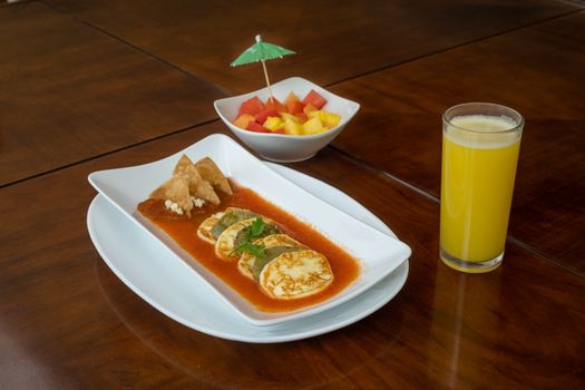 Traditional Mexican breakfast with eggs in salsa, served with fruit salad and juice.