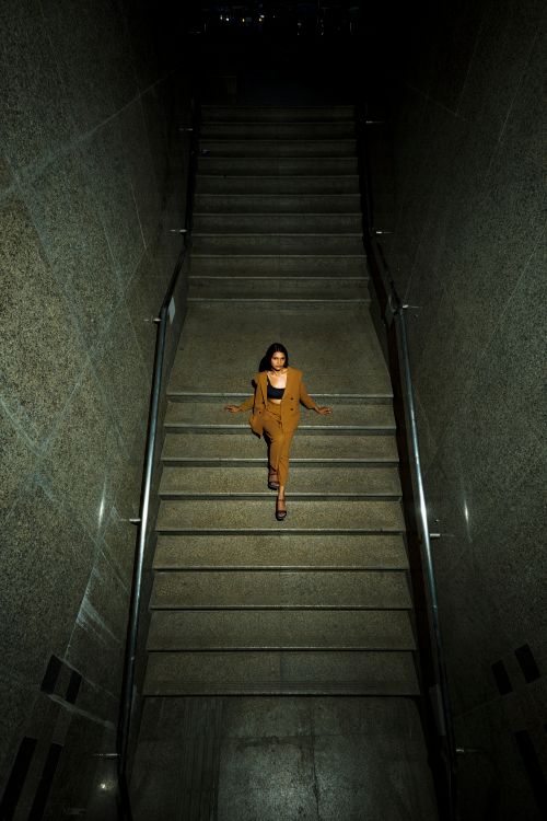 Free A fashionable woman in brown clothes confidently walks down a dramatic staircase. Stock Photo