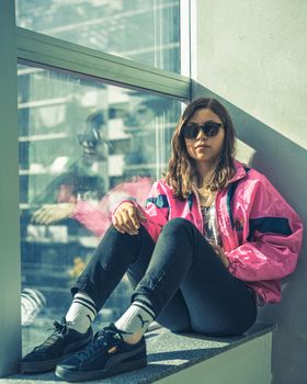 Young woman in pink jacket and sunglasses sitting by a window in Buenos Aires.