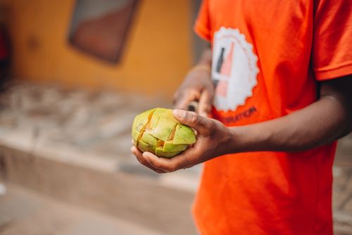Free A man in an orange shirt skillfully peels a mango outdoors, highlighting street life. Stock Photo