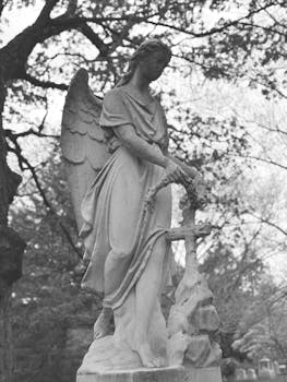 Black and white photo of an angel statue in a serene outdoor cemetery setting.