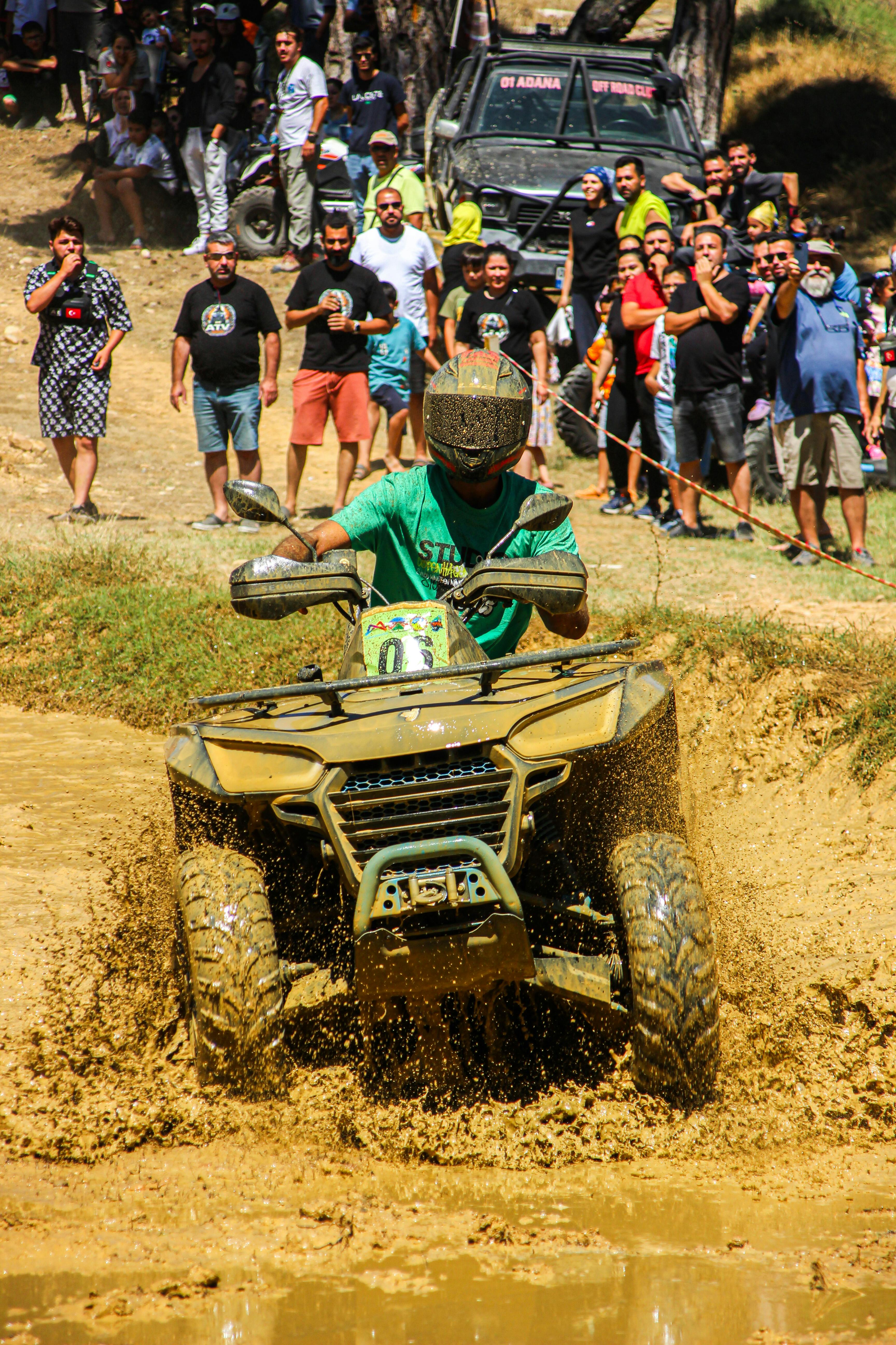 Thrilling action shot of an ATV rider splashing through mud, surrounded by onlookers during an off-road race.