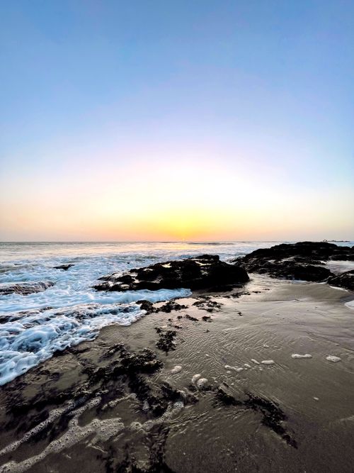 Free A tranquil beach scene at sunrise with waves crashing on rocky shores. Stock Photo