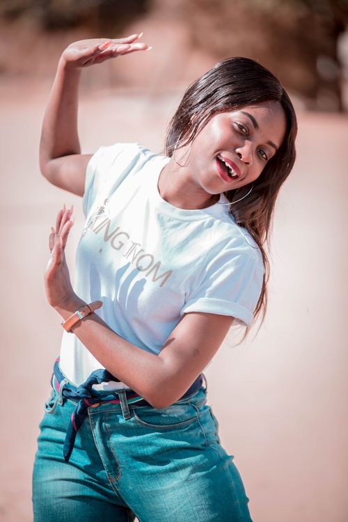 Free Lively young woman in casual attire joyfully posing outdoors on a sunny day. Stock Photo