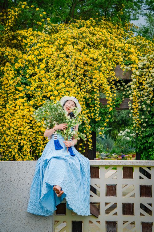 Free Woman in a blue dress enjoying a floral environment with vibrant yellow roses in the background. Stock Photo