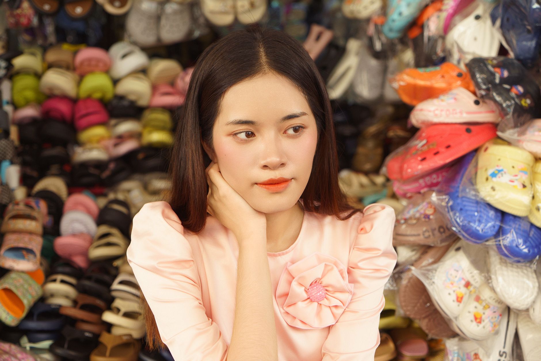 A Vietnamese woman in traditional attire at a vibrant street market surrounded by footwear.