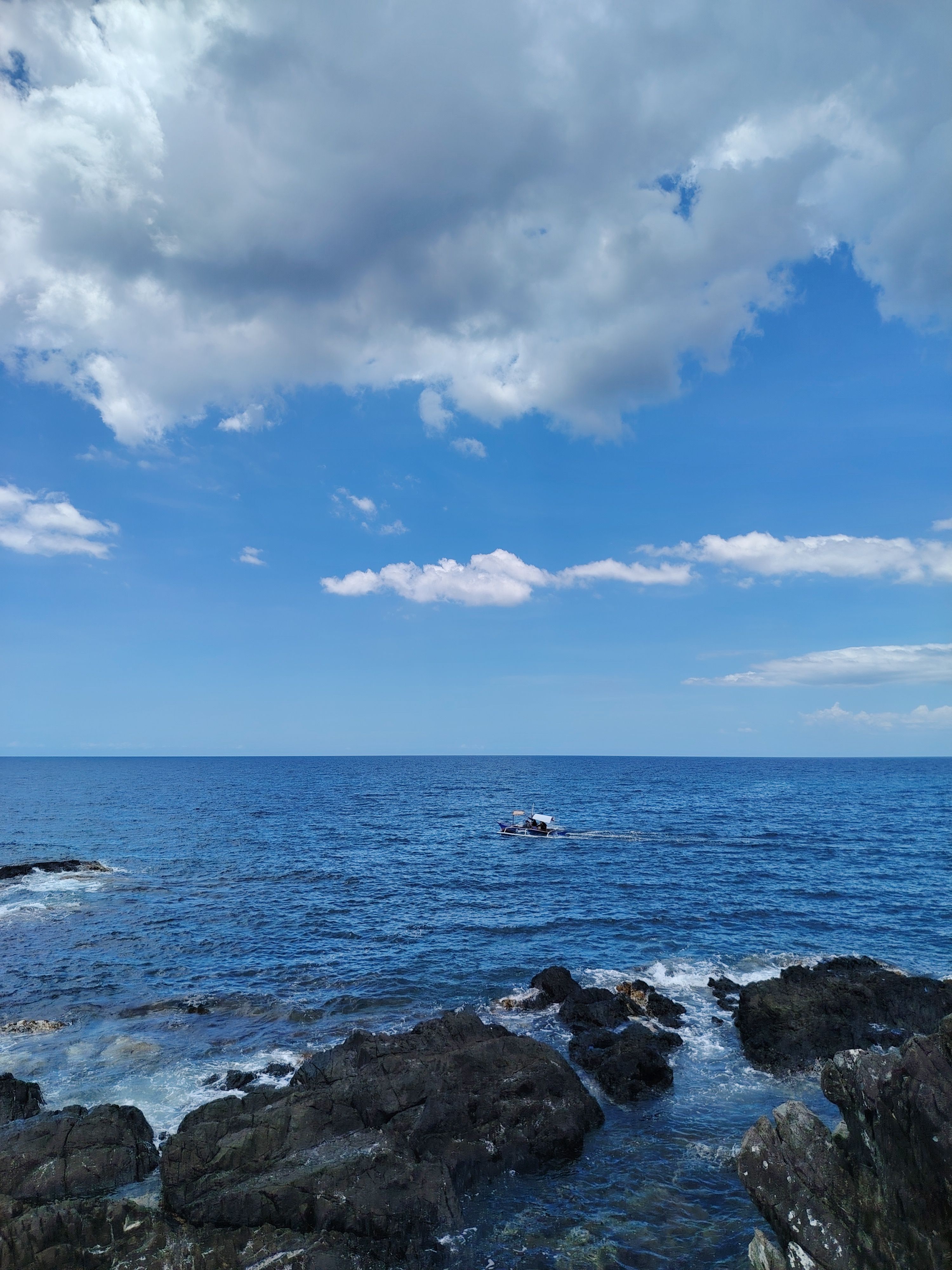 Rocky Coastline with Distant Boat Under Blue Sky