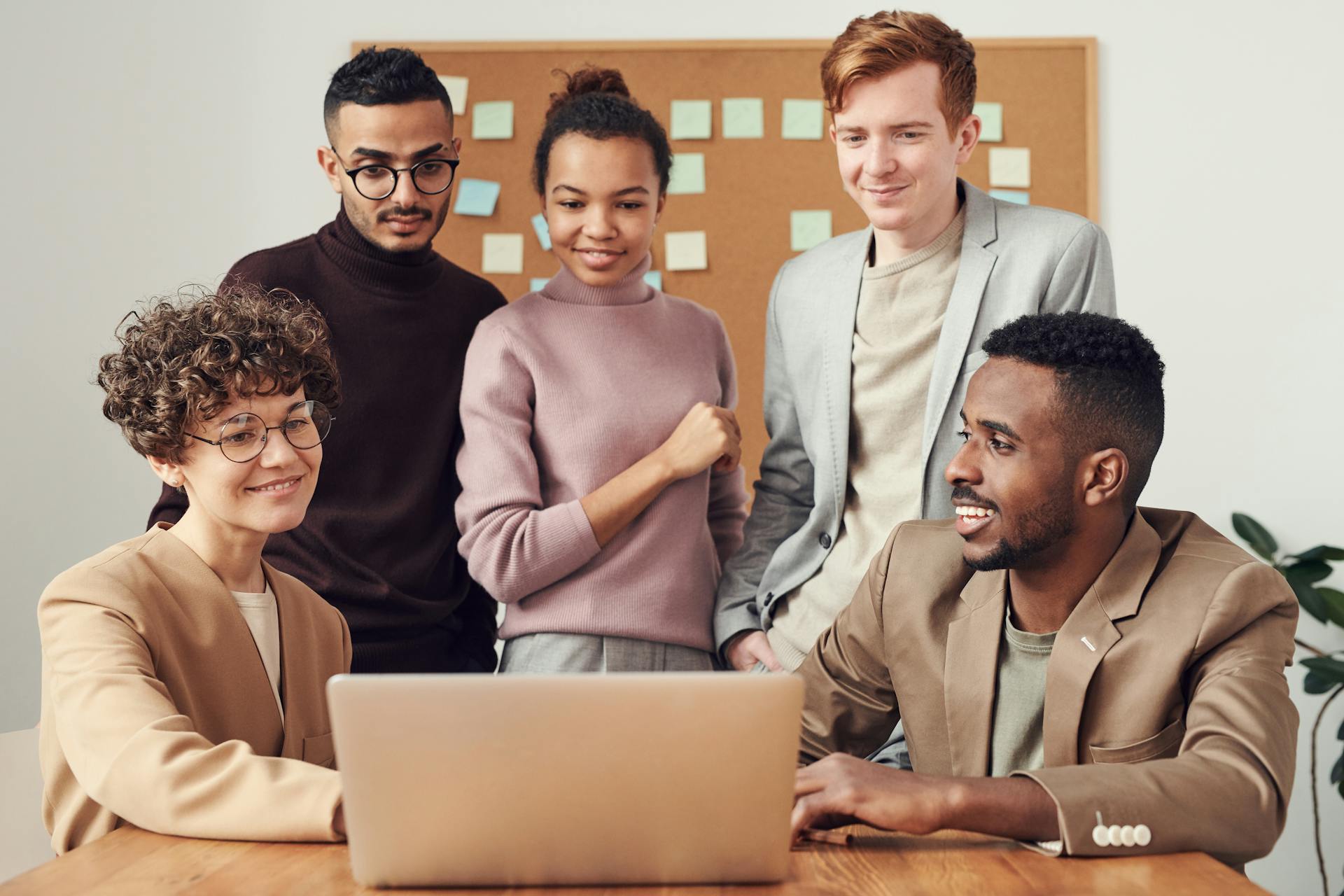 A diverse group of professionals collaborating around a laptop in an office setting.