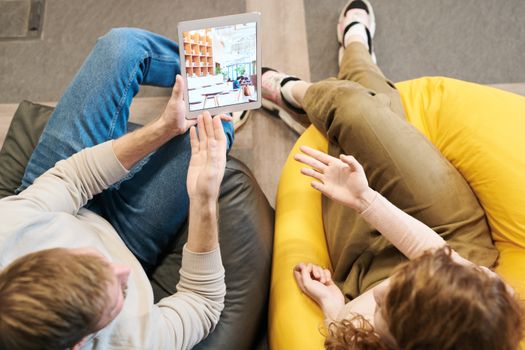 Two adults discussing content on a tablet while sitting on bean bags indoors. - Fotografer Sidoarjo