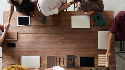 Group of adults having a business meeting, discussing plans around a wooden table with tech devices.