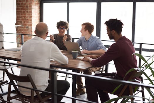 Four diverse team members collaborate around a wooden table in a modern, indoor office setting.