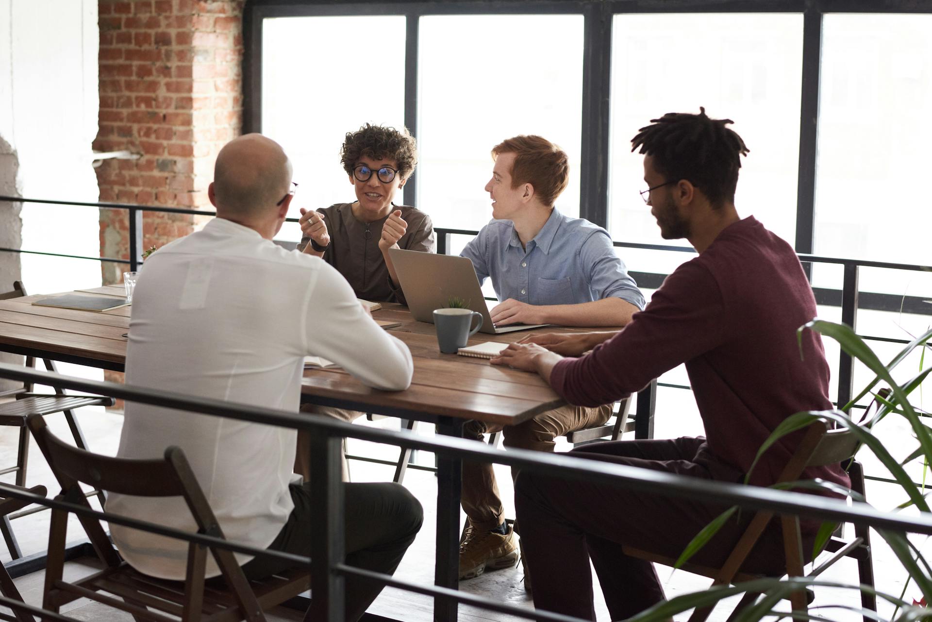Four diverse team members collaborate around a wooden table in a modern, indoor office setting.
