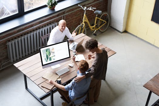 Three colleagues collaborate in a stylish office setting, discussing projects with enthusiasm around a computer.
