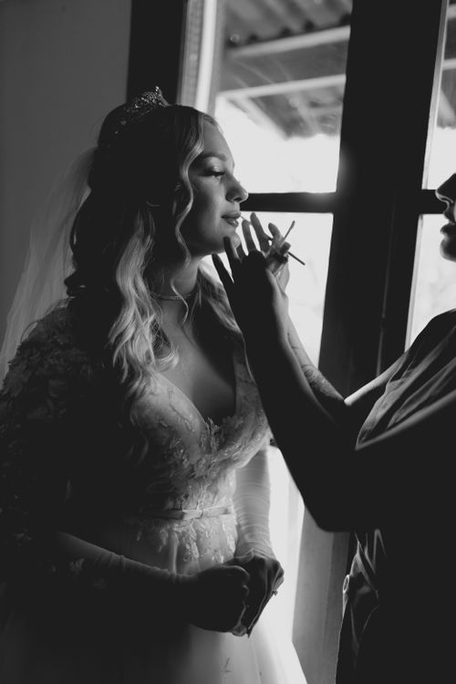 Free Bride in elegant gown getting makeup done, silhouetted by window light. Stock Photo