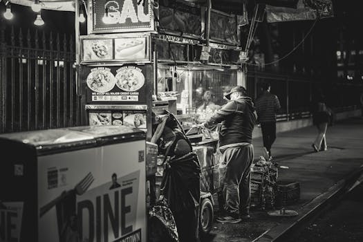 Black and white photo of a food vendor in New York City, capturing urban night life.