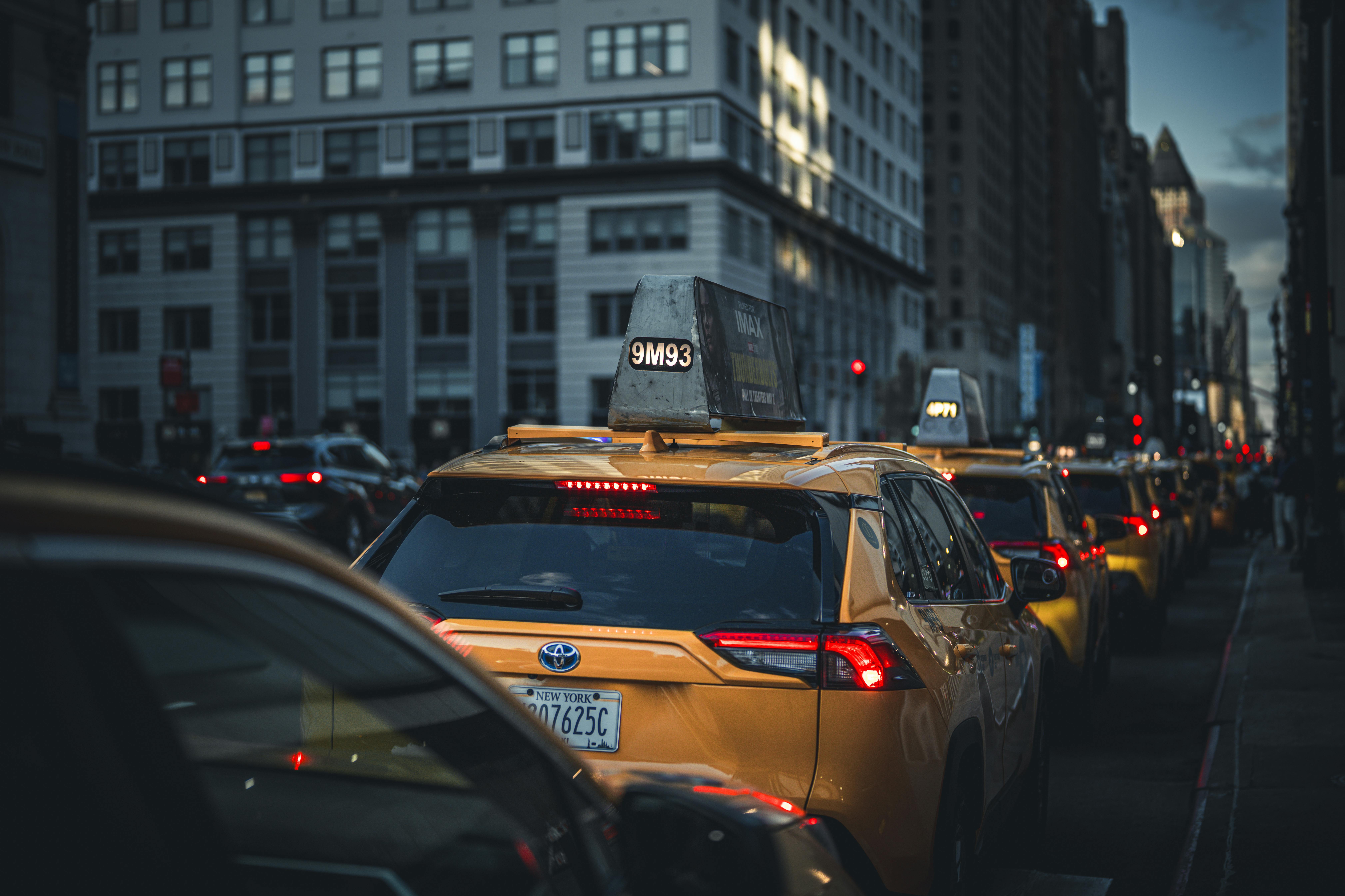Yellow taxis lined up on a bustling New York City street during evening rush hour, capturing urban life.