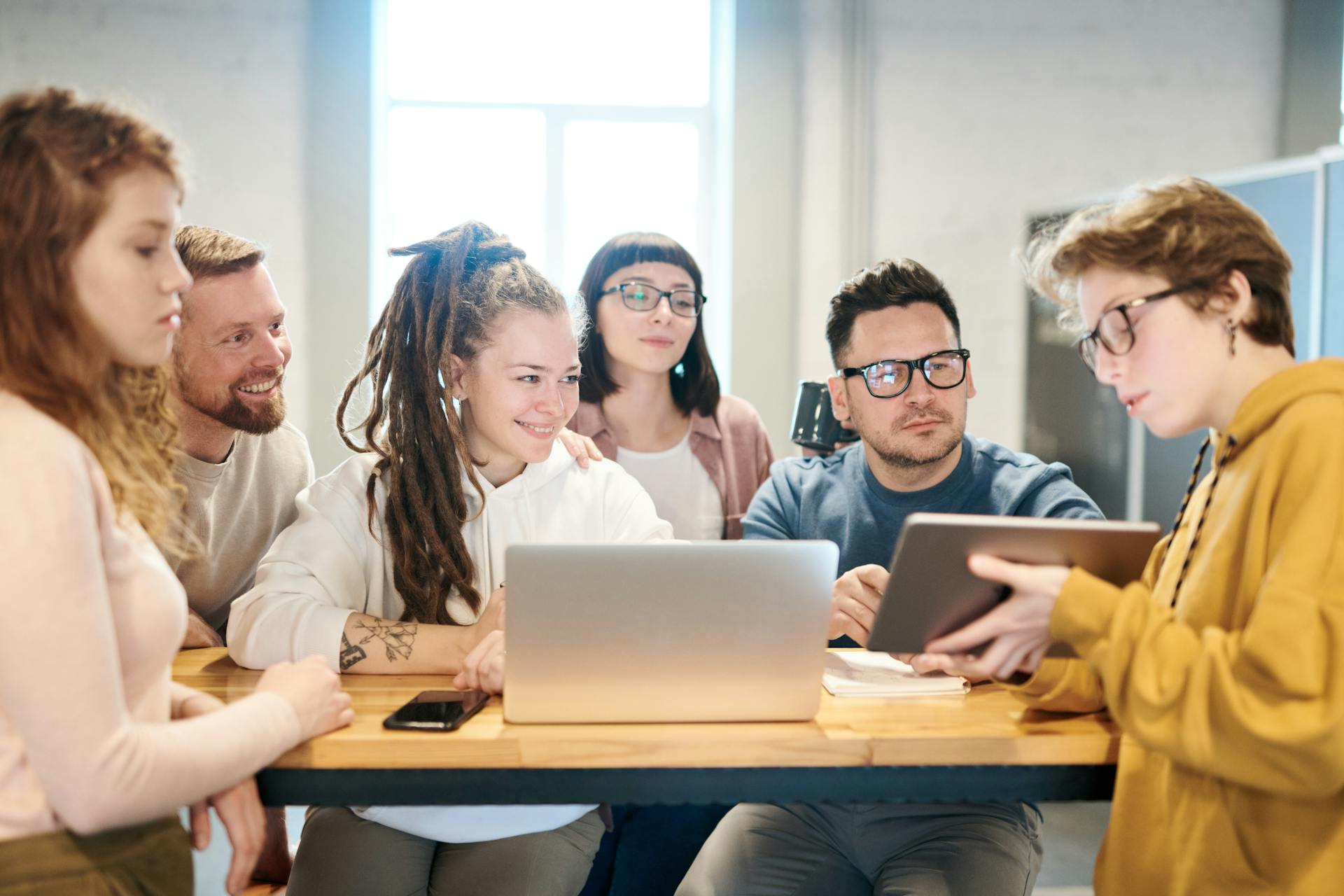 A diverse group of professionals engaged in a brainstorming session around a wooden table with technology present.