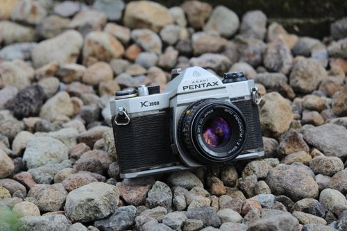 Free A classic Pentax camera rests on rocky ground in an outdoor setting. Stock Photo