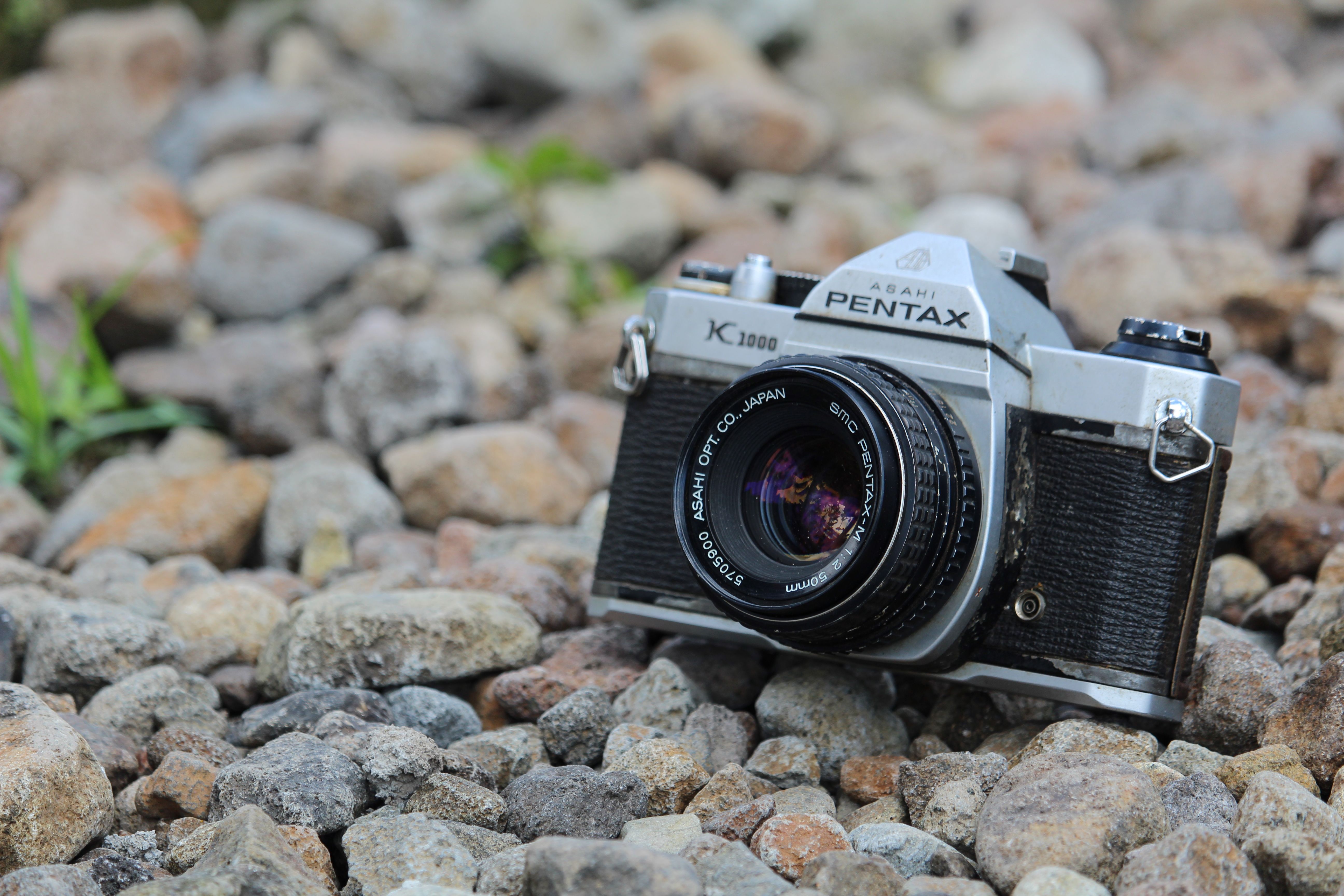 Close-up of a vintage Pentax camera resting on a bed of rocks, showcasing classic design.