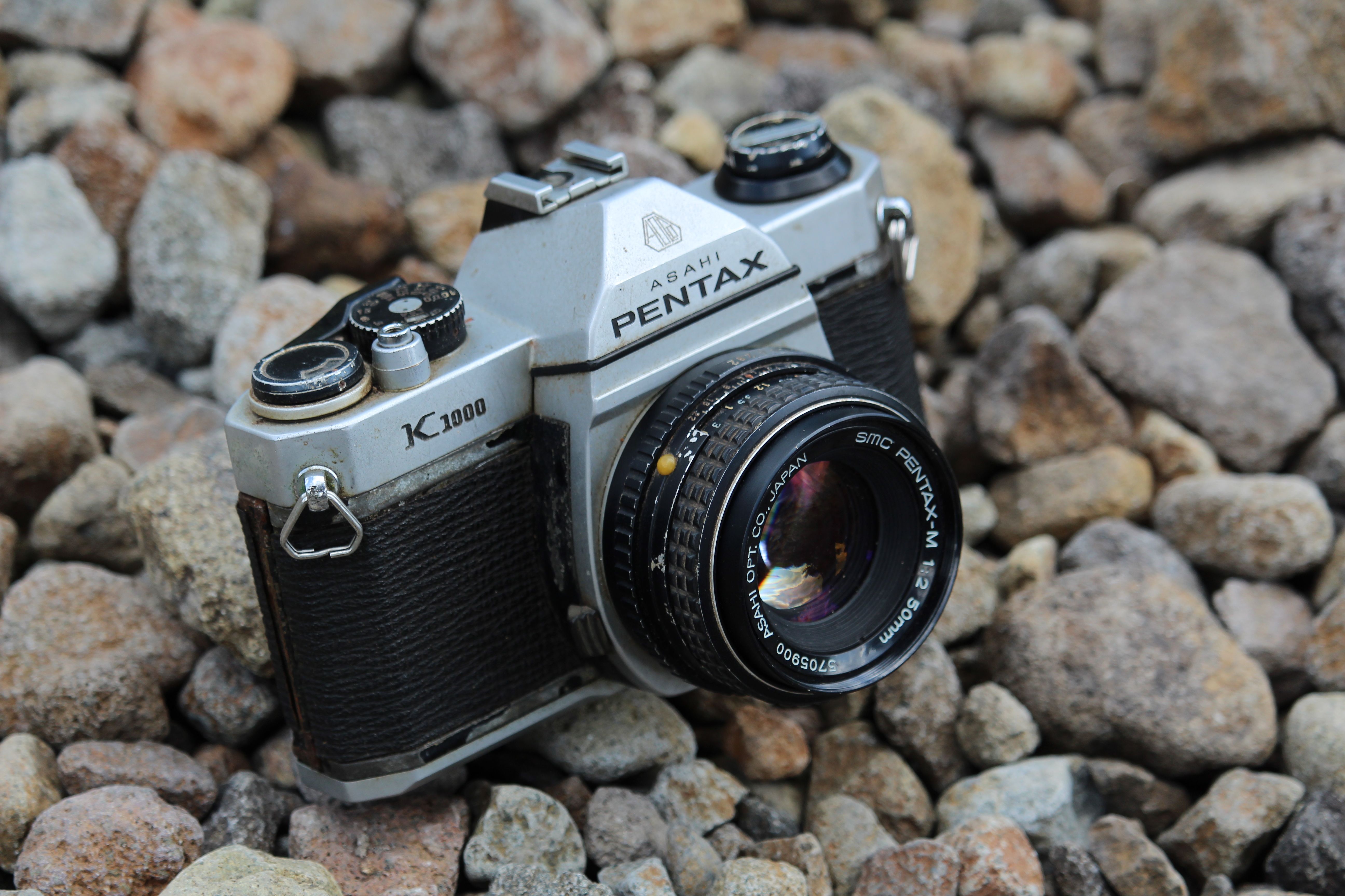 A classic Pentax K1000 camera resting on a bed of stones in Indonesia.