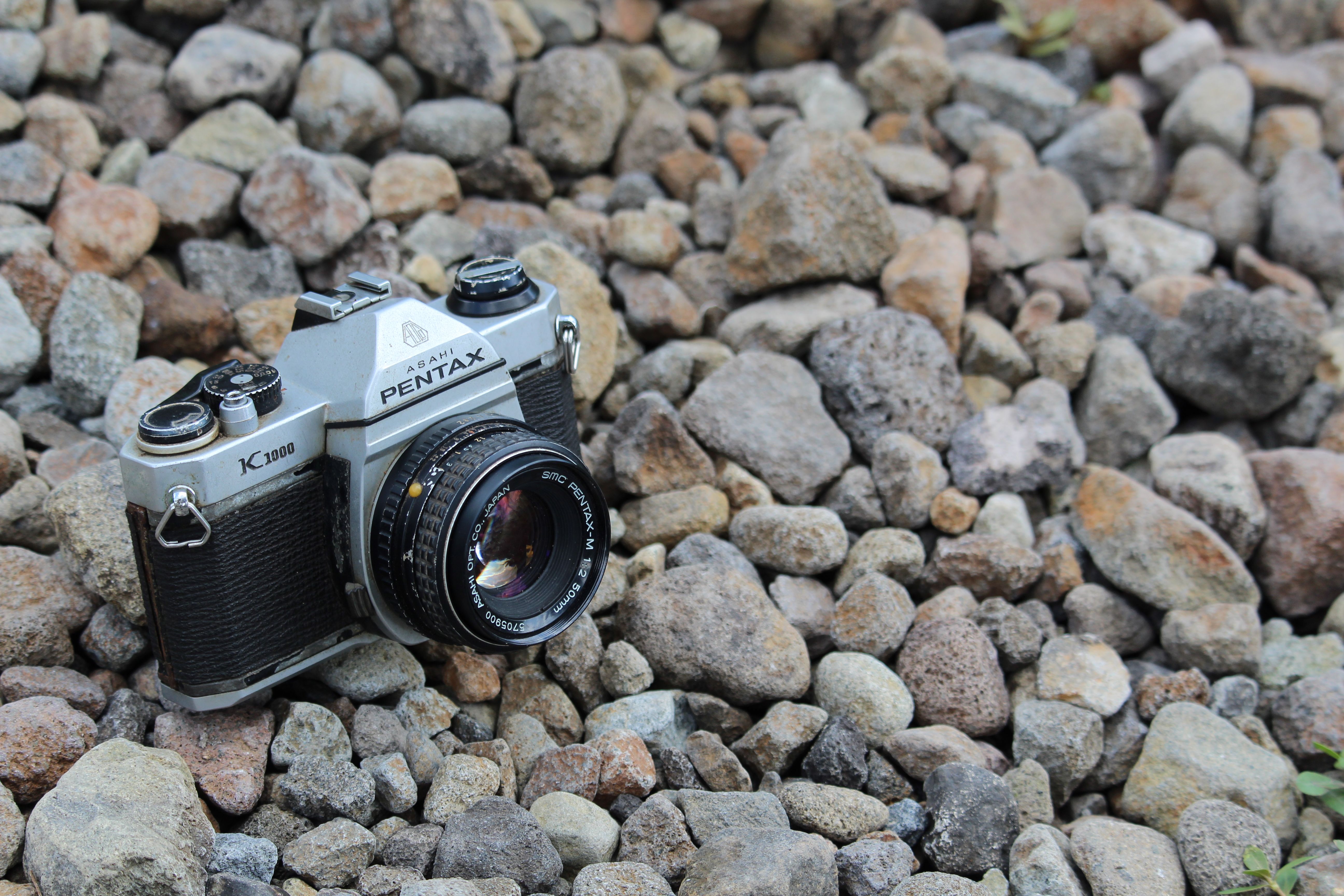 Close-up of vintage Pentax Asahi K1000 camera resting on scattered rocks, depicting retro photography charm.