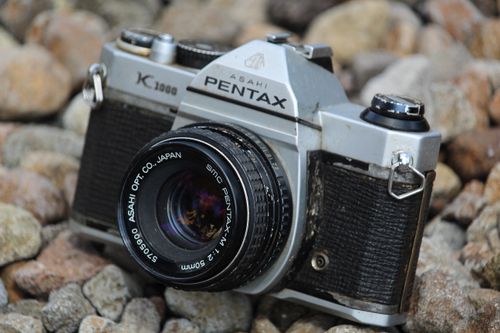 Free Close-up of a classic Asahi Pentax K1000 camera resting on rocks, showcasing its vintage design. Stock Photo