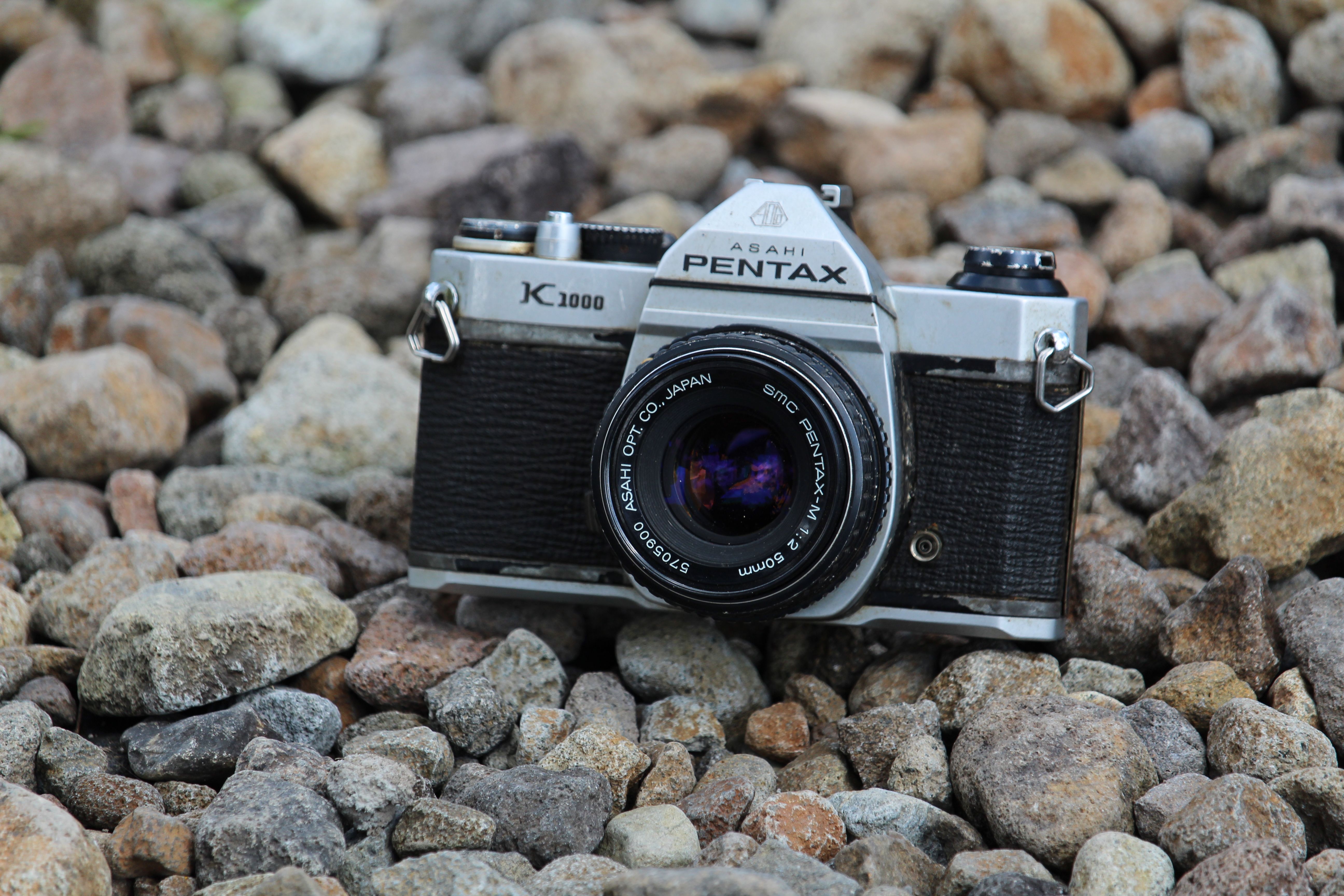 A classic Pentax Asahi K1000 camera rests among stones, showcasing timeless elegance in Indonesia.